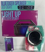 Four Proscan branded electronic items: Bluetooth speaker LED light box, light-up Bluetooth speaker box, Proscan portable CD player in plastic packaging, and Proscan AM/FM radio box.