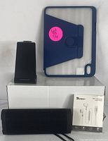 Full lot setup showing all 4 items: a black Bluetooth speaker, wireless charging stand, Energe headphones box, and blue tablet case.