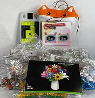 View of the lot showing children's headphones with fox design, flower building toy kit box and pieces, children's alarm clock box, and WiSlide game controller
