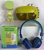 Full lot showing dinosaur bubble machine, dinosaur alarm clock, boxed children's calculator, and blue children's headphones on white background.