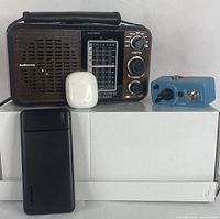 Lot showing the Audiocracky retro radio, white wireless earbuds case, Donner blue guitar pedal, and black powerbank arranged on a white box