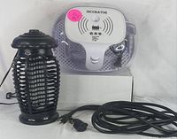 Photo showing the digital egg incubator with temperature display on top, a black bug zapper with protective electric grid, and a coiled black electrical cord with plug.