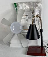 Black LED candle lamp with brass neck, red base next to white ceiling fan blades and Hoomee air seal kit in plastic packaging.