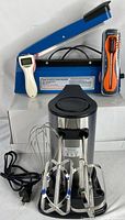 Photo showing all four items: hand mixer with two beaters and whisk, digital meat thermometer, electric can opener, film sealer