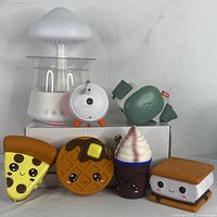 White cool mist humidifier with transparent water tank and mushroom top, alongside green wireless noise-cancelling baby headphones and round white noise machine on box, with five colorful food-shaped baby toys in front.