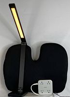 Photo shows the black memory foam seat cushion with contoured ergonomic shape, mesh fabric, black adjustable LED desk lamp lamp head and arm, and compact white power strip with attached cord and four outlets with three USB ports on the front