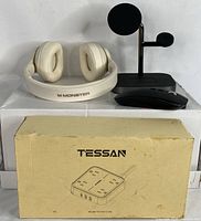 White Monster wireless headphones next to black 3-in-1 wireless charger stand and black powerbank in front of a Tessan box.