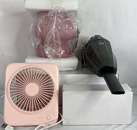 Pink compact USB-powered desk fan, black cordless handheld vacuum with nozzle, all shown with packaging boxes, placed on white surface.