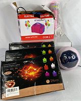 Image shows the electric balloon pump in its original box with some additional items including three boxes of colorful LED tea lights and the karaoke microphone.
