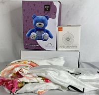 Lot contents showing boxed blue Starry Night projector teddy bear, boxed travel noise machine, and folded baby milestone blanket