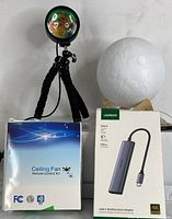 Sunset lamp on flexible tripod, LED globe light on wooden stand, USB-C Ethernet adapter, and ceiling fan remote control kit in package.