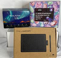 Three boxed items: Wacom CTL-672 tablet in brown box, Music Aurora Lamp in blue box, UV Resin Starter Kit in multi-colored box.