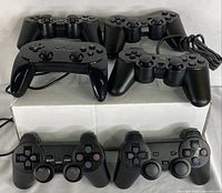 Photo showing six black gaming controllers arranged on and in front of a box, featuring both wired and wireless models with various control button layouts.