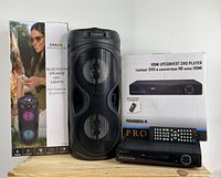 Bluetooth party speaker with LED lights alongside Proscan HDMI upconvert DVD player, box, remote, and manual on wooden surface.