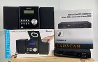 Sylvania Bluetooth CD Micro System and Proscan HDMI DVD player with their original boxes and remotes displayed on a wooden surface.