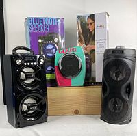 Photo of two black Bluetooth party speakers with LED lights alongside a portable CD player in front of packaging boxes.