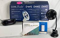 Photo showing all items together: Luxe Neo 120 Blue bidet box, digital alarm clock on white box, essential oil diffuser box, Lutron Pico remote control box, and black mini fan.