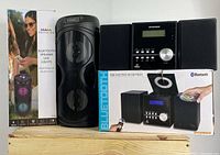 Proscan Bluetooth party speaker with LED lights beside the Sylvania Bluetooth CD micro system stereo and its box all set on a wooden crate.