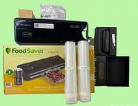 Black FoodSaver FM2010 vacuum sealer on top of its branded yellow box along with two rolls of vacuum sealing bags and packaging waste.