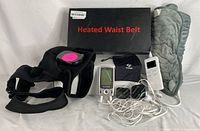 Complete set of the heated waist belt, TENS stimulator with cables and electrodes, heating pad, and heated shoulder brace laid out on a white background.