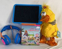 Lot contents showing blue and orange LCD writing tablet, boxed Light-Up Terrarium Kit, children's blue and orange headphones, and yellow plush quacking musical duck