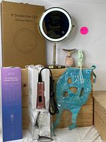 Photo of all items showing makeup mirror next to original box, hair curler in packaging, blue gel mask, beauty massager and USB fan.