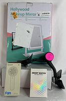 Photo showing the front of the Hollywood Makeup Mirror box along with the thigh strength trainer device, the mini fan box, and the smart watch box.