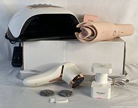 Front view showing LED nail lamp, automatic hair curling iron, and electric callus remover with accessories arranged on white box.
