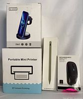 Four boxed electronic items: portable mini printer, rechargeable wireless mouse, 3-in-1 wireless charger (CW350), and stylus pen.