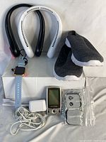 Full lot view showing smart watch with charger, TENS massager with electrode pads and charger, two neck fans (black and white), and black walking shoes.