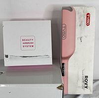 White box labeled 'Beauty Airbrush System' next to a larger pink and white box for TYMO Rovy wave curling iron.