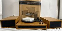 Front view of vintage-style wooden turntable with two matching speakers and original box behind it. Styrofoam packing on platter.