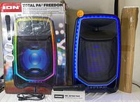 Boxed ION Total PA Freedom portable speaker with wireless microphone and power cable included, LED lit speaker front visible.