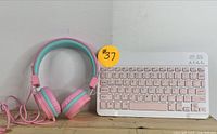 Wireless keyboard and wired headphones set on wooden surface, both in good condition with pink and white color scheme for keyboard and pink and teal for headphones.