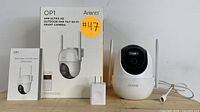 Full lot contents including security camera, original box labeled 'OP1 4MP Ultra HD Outdoor Pan Tilt WiFi Smart Camera', power adapter, and quick guide manual arranged on a white surface.