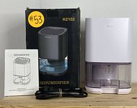 Dehumidifier with original box, manual, and power cord displayed on wooden surface