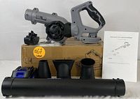 Leaf blower main unit balanced on box, showing multiple nozzle attachments and instruction manual.