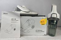 White Dibea UV-10 handheld vacuum cleaner with instruction manual and packaging box marked UV Mattress Vacuum Cleaner.