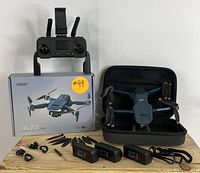 Drone, remote, box, batteries, propellers, and carrying case on wooden surface.