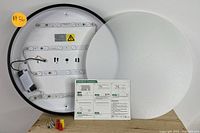 Round LED ceiling light with frosted cover and mounting hardware laid out, showing internal LED strips and wiring components with an instruction sheet.