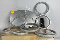 Photo showing four circular LED light rings of different sizes, black remote control, and mounting hardware on a wooden surface.