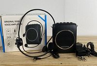 Portable voice amplifier with headset microphone and packaging box on wooden surface.