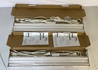 Two boxed under cabinet LED light fixtures with power cords and manuals laid out on a flat surface.
