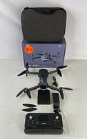 Image showing the NT V11 Pro drone unfolded with all four propellers extended, two spare batteries, remote control and gray carrying case on top of the original box.