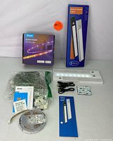 Photo of the full set including boxed Govee LED strip light, boxed FULEN motion sensor lights, LED strip roll, motion sensor light bars, USB cables, mounting accessories, and manuals on a flat surface.