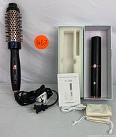 Heated styling brush with vented barrel and bristles, power cord coiled beside it, and cordless hair curler in box with accessories laid out.