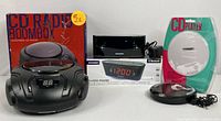 Photo of entire bundle showing CD radio boombox, digital alarm clock, black portable CD player, and packaged white portable CD player with power cords and accessories.