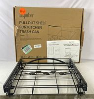 Black metal pull-out shelf with sliding rails placed upright, shown with assembly instructions and original box behind.