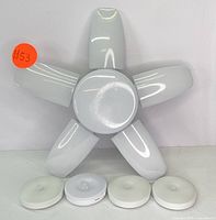 Foldable LED ceiling light with five white panels radiating from a central hub alongside four round wireless puck lights placed below.