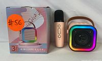 Photo showing wireless microphone and Bluetooth speaker placed beside its retail box with product illustration and orange sticker.